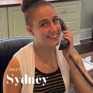 Sydney answers a phone and smiles at the person taking a photo