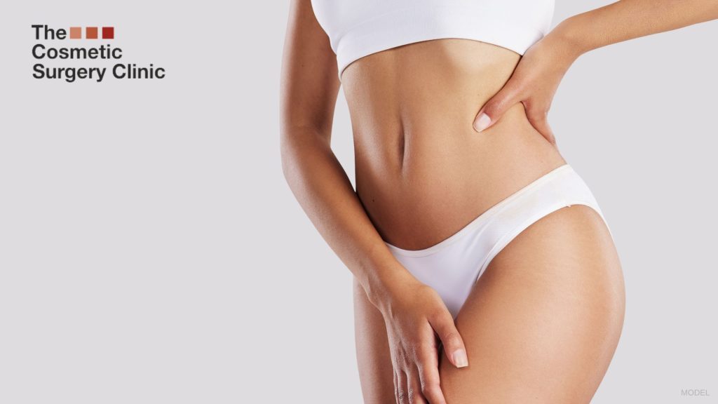 A woman's stomach with their hands on their hips. (Model)
